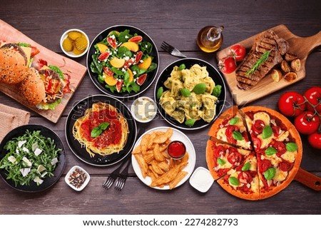 Table scene with a variety of delicious foods. Above view over a dark wood background.