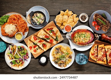 Table scene of various delicious foods. Top down view on a dark wood background. Pastas, flatbreads, tacos, steak and restaurant theme dishes. - Powered by Shutterstock