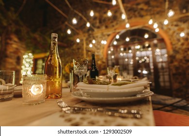 Table Served For Dinner Party Outdoors In Evening With Lights In Background. Beautiful Table Setting For A Big Party In The Night.