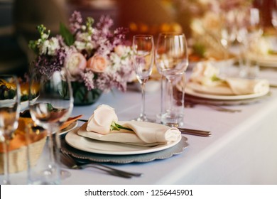 Table Served For Special Occasion. Empty Plate, Glasses, Forks, Napkin And Flowers On Table Covered With White Tableclothes. Elegant Dinner Table. White Table Setting