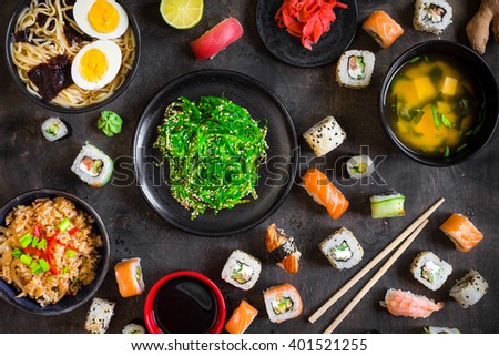 Table served with sushi and traditional japanese food on dark background. Sushi rolls, hiyashi wakame, miso soup, ramen, fried rice with vegetables, nigiri, soy sauce, Chopsticks. Overhead



