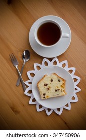 Table served to tea drinking. White cup of tea, paper napkin, cutlery and cake with raisins on the wooden table.