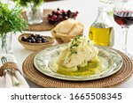Table set for a dinner, with green decorated portuguese plate, glass of wine and some side dishes. A codfish with potatoes, onion and parsley is being served, an typical portuguese dish.