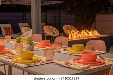 A table set for dinner outdoors at night with a cozy fireplace - Powered by Shutterstock