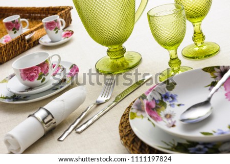 Table set up with dinnerware, napkin, silverware, jar and cups of glass on table cloth