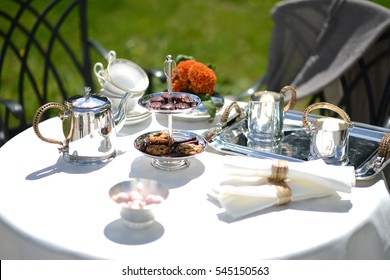 Table Set For An English High Tea, Or Afternoon Tea, Outside With Silver Teapot And Linen Tablecloth