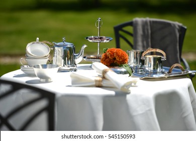 Table Set For An English High Tea, Or Afternoon Tea, Outside With Silver Teapot And Linen Tablecloth