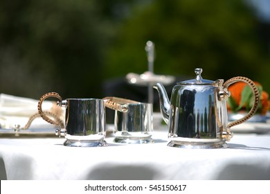 Table Set For An English High Tea, Or Afternoon Tea, Outside With Silver Teapot And Linen Tablecloth