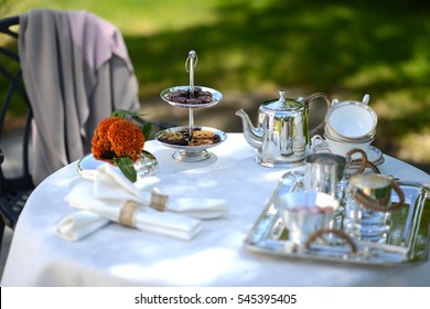 Table Set For An English High Tea, Or Afternoon Tea, Outside With Silver Teapot And Linen Tablecloth