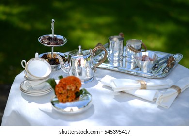 Table Set For An English High Tea, Or Afternoon Tea, Outside With Silver Teapot And Linen Tablecloth