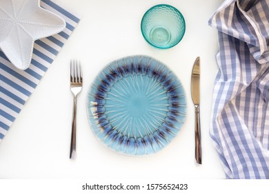 Table set in marine style - empty plates in shape of starfish, blue glass, fork and knife on striped napkins on white background. Preparation to table setting. Flat lay, top view, copy space - Powered by Shutterstock