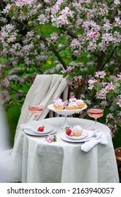 Table Set On A White Tablecloth On A Sunny Day, Cherry Blossom, Cupcake, Wine. Outdoor, Picnic, Brunch, Spring Mood. Soft Focus