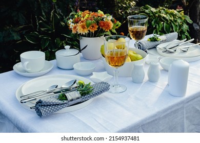 Table set for outdoor eating on a table in the garden. Elegant table setting with white dishes on a white linen tablecloth. Sunny day light. Copy space