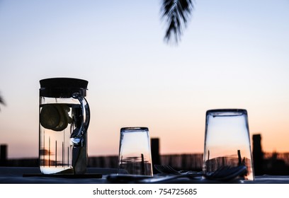 Table Set Outdoors At Splendid Sunset With Water Jar And Glasses Upside Down. Dinner On Countryside At Twilight