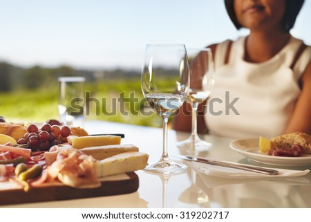 Table set in the winery with two glasses of wine, cheese and grapes. Woman sitting in back at winery restaurant table.