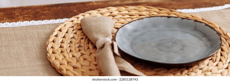 Table setting in authentic design and rustic style. Ceramic plate on a wicker stand with a linen napkin. Banner for website header design with copy space.