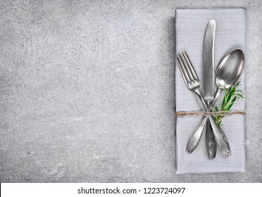 Table setting background with copy space. Concrete background with napkin, silverware and rosemary branch. Cutlery with fork, knife and spoon. Top view.