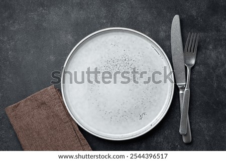 Table setting with empty plate and cutlery on black stone background. Copy space for design or text
