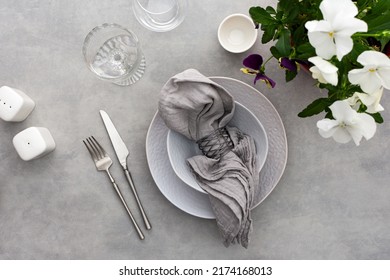 Table setting, empty plate with napkin and cutlery on the on the gray background, top view of the served table decorated with pansies flowers