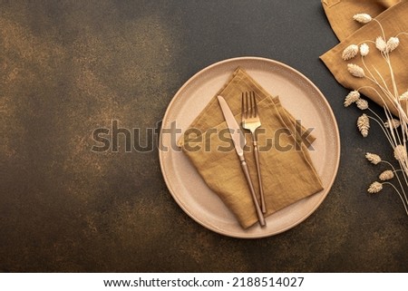 Table setting, empty plate with napkin and cutlery on a brown background, top view of the served table decorated with dry flowers