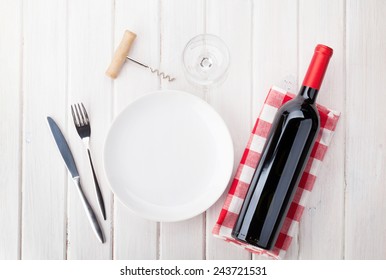 Table Setting With Empty Plate, Wine Glass And Red Wine Bottle. View From Above Over Rustic Wooden Table Background