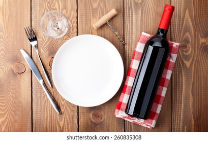 Table Setting With Empty Plate, Wine Glass And Red Wine Bottle. Top View Over Rustic Wooden Table Background 