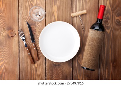 Table Setting With Empty Plate, Wine Glass And Red Wine Bottle. Top View Over Rustic Wooden Table Background