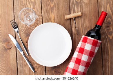 Table Setting With Empty Plate, Wine Glass And Red Wine Bottle. Top View Over Rustic Wooden Table Background