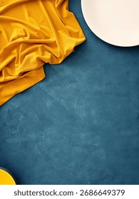 Table setting featuring a white plate, fork, knife, and yellow napkin on a blue background. Minimalist flat lay for food mockup setting with copy space.