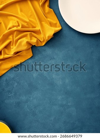 Table setting featuring a white plate, fork, knife, and yellow napkin on a blue background. Minimalist flat lay for food mockup setting with copy space.