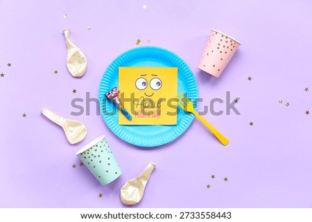 Table setting with festive postcard, confetti and party decor for April Fools Day on lilac background