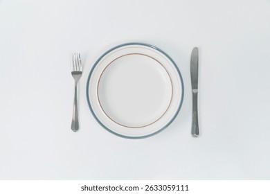 Table setting with a fork and knife next to an empty plate on a white table