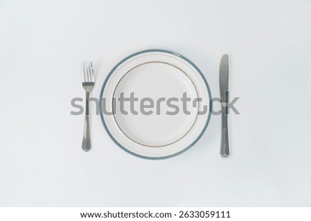 Table setting with a fork and knife next to an empty plate on a white table