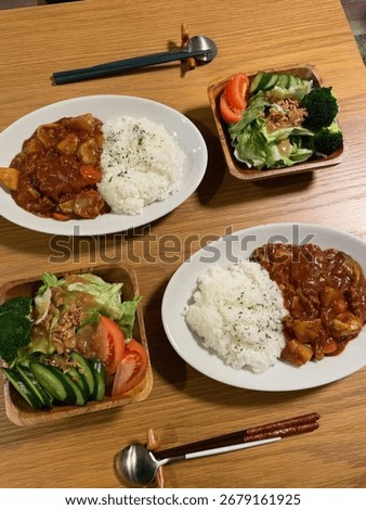 A table setting with four plates of food.  Each plate contains curry, rice, and a side salad.  The food appears to be ready to eat.