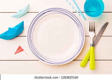 Table Setting For Kids. Empty Plate On White Planked Wooden Table With Colorful Decorations Around - Captured From Above (top View, Flat Lay).