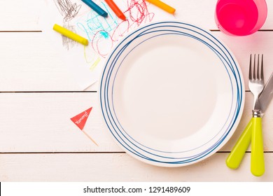 Table Setting For Kids. Empty Plate On White Planked Wooden Table With Colorful Decorations Around - Captured From Above (top View, Flat Lay). Layout With Free Text (copy) Space.