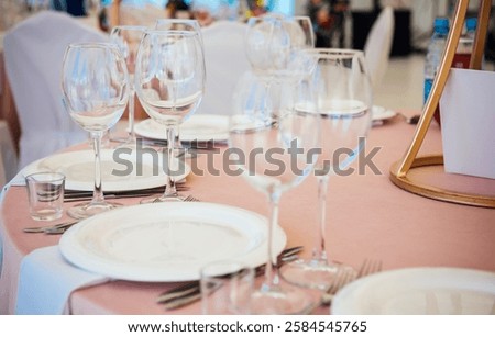 Table setting with light pink tablecloth close up. Wine and beverage glasses, white plates, forks and knives, preparation of the restaurant for the reception of guests.