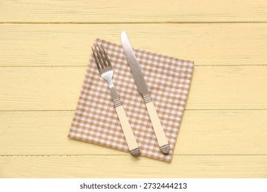 Table setting with napkin, fork and knife on yellow wooden background