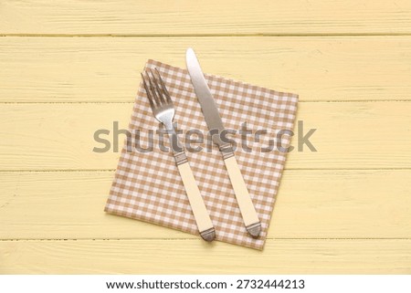 Table setting with napkin, fork and knife on yellow wooden background