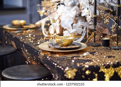 table setting with plates, silverware, gift box and decorations in black and gold colors