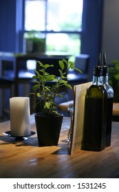 A table setting in a restaurant consisting of bottles of olive oil and vinegar with a pot of mint on wooden table