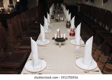 Table Setting In The Restaurant. White Tablecloth, Napkins, Glasses, Plates And Knives With Forks, Surrounded By Wooden Glasses. The Concept Of Preparation For A Celebration Or Party.