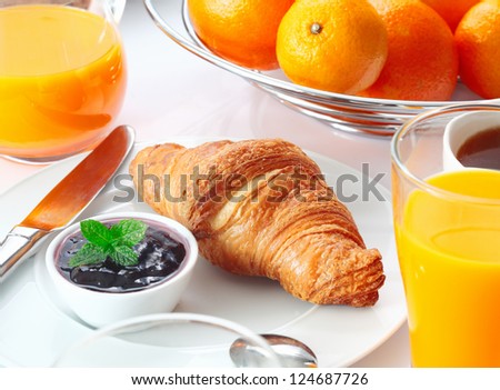 Table setting with a tasty Continental breakfast including fresh oranges and orange juice, strawberry jam and a crisp flaky croissant
