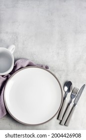 Table setting. White plate, mug, cutlery and napkin on light gray background. Flat lay, top view, copy space.