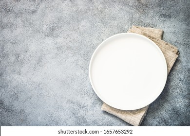 Table setting with white plate and napkin at stone background. Top view on kitchen table.