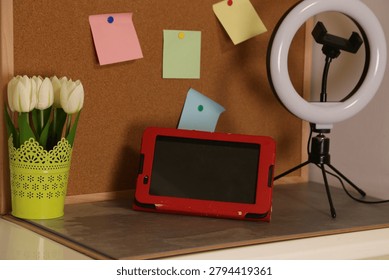 Table setup with a tablet, a lamp, flowers, and notes in a workspace during the day