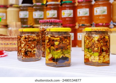 A table with several jars of nuts and fruit. The jars are all different sizes and are filled with various types of nuts and fruit, walnuts in honey