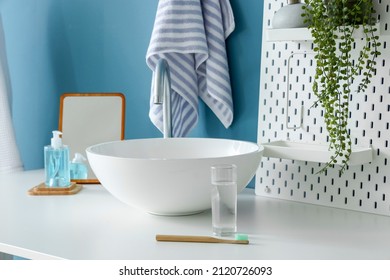 Table With Sink, Glass Of Water, Toothbrush And Pegboard Near Blue Wall