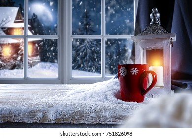 Table With Space For Your Product Or Advertising Tex. Candle Lamp Giving Warm Light. Window Overlooking The Winter Mountains And The Moon In The Sky.