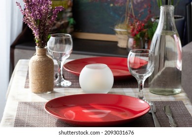 Table With Tableware: Empty Without Meal Red Plates, Wine Glasses, Bottle For Water And Knife And Fork For Romantic Dinner For Two Persons At Home